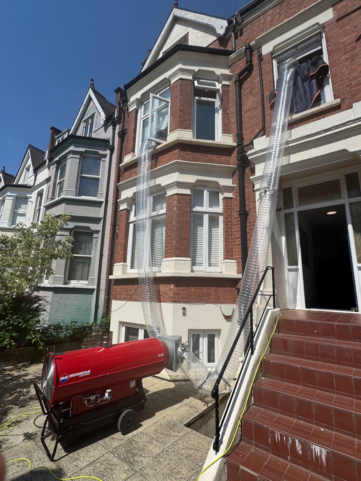Two heat-treatment ducts running from an industrial heater up into the front bay window of a London townhouse