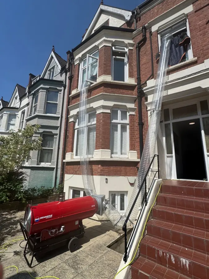 Two heat-treatment ducts running from an industrial heater up into the front bay window of a London townhouse